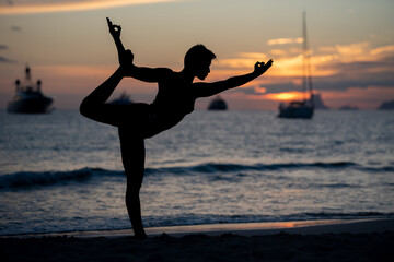 Silhouette of Fitness model doing yoga at sunset time.
