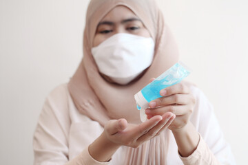 Muslim woman wearing a surgical mask washing hands with alcohol gel on pastel background. Covid-19 coronavirus concept.