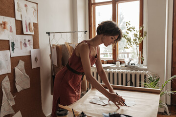 Beautiful young short-haired woman in red linen dress works as fashion designer. Attractive lady...