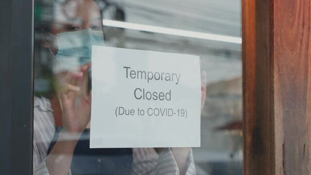 Caucasian Coffee shop owner wear mask, turns Temporary closed sign.