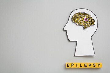 Human head cutout, brain and yellow cubes with word Epilepsy on light grey background, flat lay....
