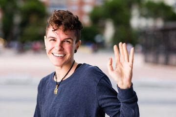 Non binary transgender Tomboy looking at camera, greeting and waving hand smiling during internet...