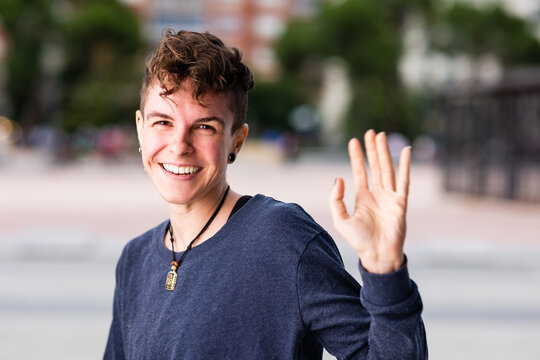 Non binary transgender Tomboy looking at camera, greeting and waving hand smiling during internet online communication.