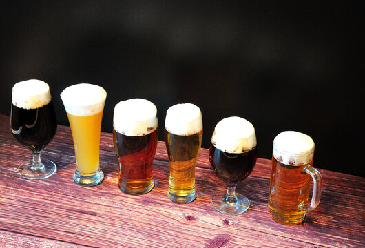 Six glasses with beer of different varieties, stand in a row on a wooden table.