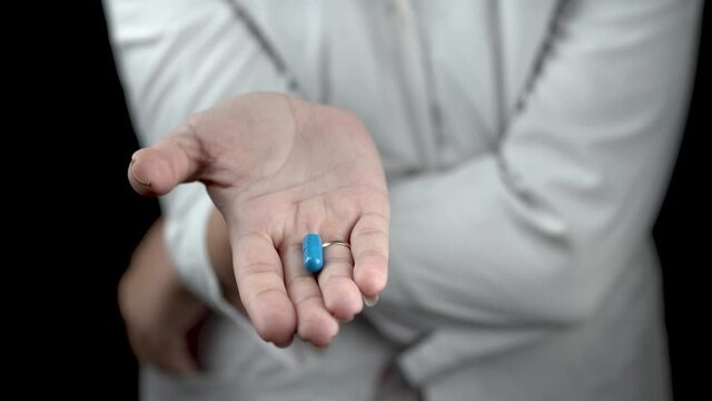 a young doctor girl in glasses holding a blue pill on a dark background