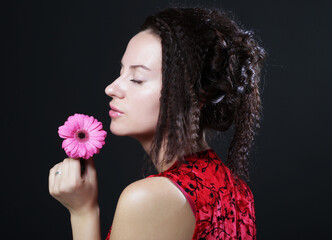 Young beautiful woman wearing red dress holding pink gerber flower