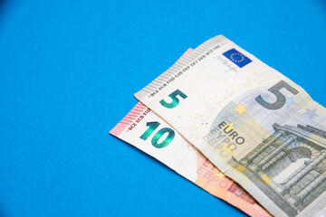 Closeup image of five and ten euro banknotes on each other at a right corner on a blue background