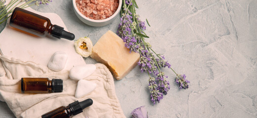 Bottle of essential oils with herbs and flowers on light gray background.