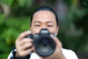 Focus on the Asian man face that he holds the blur Medium Format Camera in his hand and prepare to shoot in front of him.