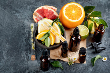 Bottles of essential aroma oils with citrus on dark gray background.