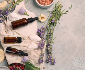 Bottle of essential oils with herbs and flowers on light gray background.