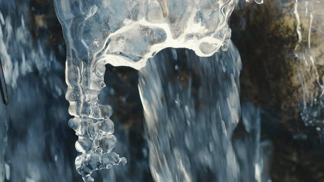 icicle in a frozen river with flowing water in background, close up, slow motion