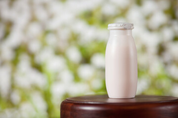 Natural liquid yogurt with probiotics in small plastic bottles on wooden table on background of meadow with flowers.
