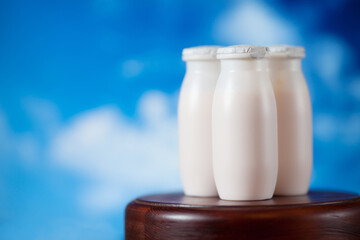 Natural liquid yogurt with probiotics in small plastic bottles on wooden table on background of green trees.