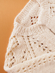 Knitted sweater made of natural beige wool, close-up. Patterns and details of knitted products. Beautiful, fashionable, cozy, women's sweater on a brown autumn background. Autumn Clothing Concept