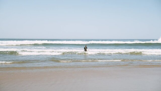 Sporty Man Holding His White Surfboard While Starting To Walk Into The Ocean Water - wide shot