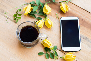 hot coffee espresso with mobile ,yellow flowers ylang ylang arrangement flat lay postcard style on...