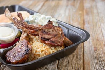 A view of a Mediterranean entree of lamb rack in a to-go container.