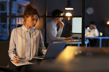 Young woman working with laptop in office at night