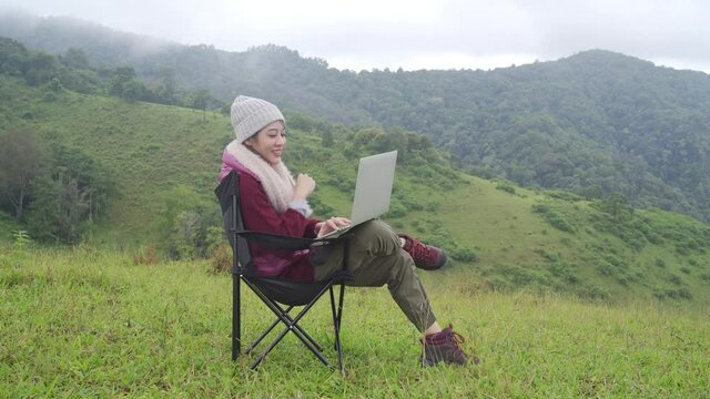 Asian businesswoman working on laptop computer for online stock trading or small business on the mountain. Modern beautiful woman enjoy outdoor lifestyle with wireless technology on summer vacation.
