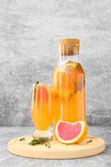 Glass and bottle of tasty grapefruit lemonade on grey background