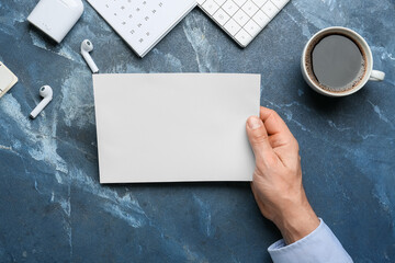 Obraz premium Male hand with blank sheet of paper, earphones and cup of coffee on color background, closeup