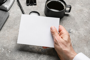 Male hand with blank sheet of paper, cup of coffee and stationery on grunge background, closeup