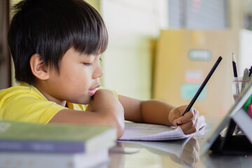 Portrait image of 7-8 years old kid. Happy Asian student child boy using and touching smart pad or tablet for do his homework and online learning (E-learning). Back to school, Study from home.