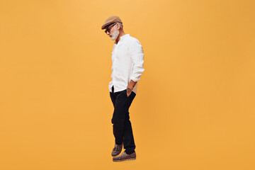 Fototapeta premium Full length portrait of man in white shirt and black pants on orange background. Photo of bearded gray-haired adult guy in fashionable clothes