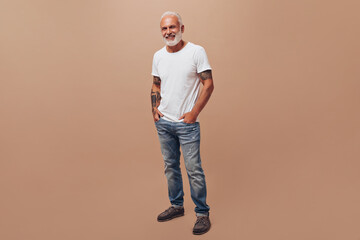 Full length shot of man in jeans and white shirt on beige background. Beautiful adult with gray...