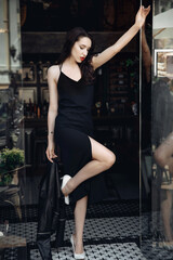 Fashion. Young stylish woman posing on the city street. Beautiful brunette stylish girl in black dress. Vertical photo.