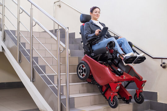 Caucasian Woman In Electric Caterpillar Wheelchair Climbs Up Stairs.