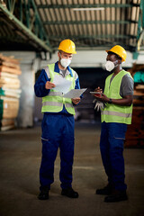 Two workers with face masks going through documents while doing stock check in warehouse.