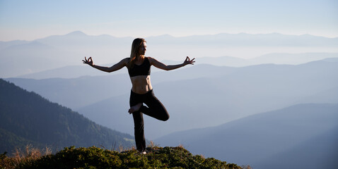 Young woman practicing yoga on background of evening mountains. Meditating female is balancing on one leg after sunset. Concept of harmony with nature.