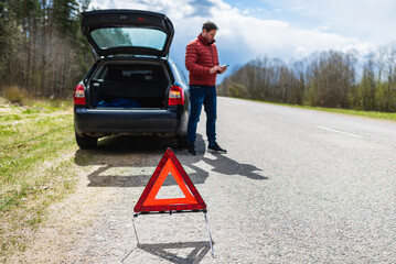 Man using the phone,smartphone in asking for help when his car is broken.Selective focus on Emergency sign.