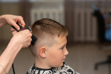 Fototapeta premium Cute kid boy have hair cut, professional barber doing haircut. Hairdress for children. side view portrait barbershop.