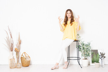 白い壁の前の椅子に座って、OKのジェスチャーをする若い女性