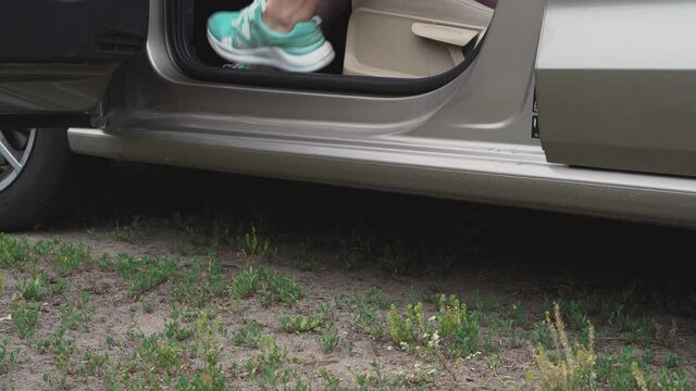 Low angle close-up shot of the feet of a young woman wearing sneakers as she opens her car door and climbs out onto the grass. The girl came to the countryside or to the forest for a walk or jog. The 