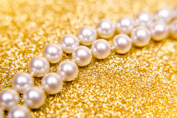 A necklace of pearls lies on a shiny gold background.
