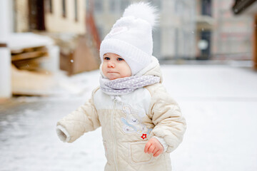 Obraz premium Happy little baby girl making first steps outdoors in winter through snow. Cute toddler learning walking. Child having fun on cold snowy day. Baby's first snow, activity. Winter walk outdoors