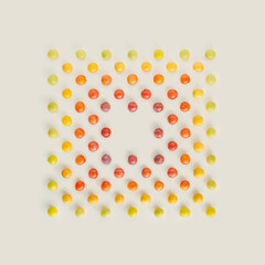 Square note card shape made of light green, yellow, orange and bold red wild plums isolated on pastel beige background. Nature inspired colorful summer fruit pattern with copy space. Minimal flat lay.
