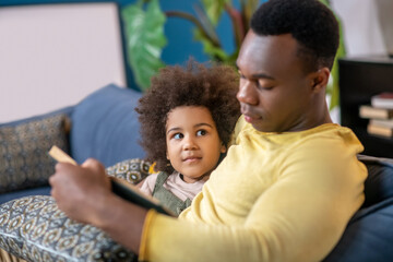 Fototapeta premium Little darkskinned girl looking at dad with book