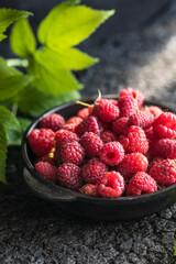 Raspberries in a  bowl on a dark wooden table, selective focus. Close-up of ripe raspberries with copy space, idea for a banner. Ingredients for raspberry juice or desserts