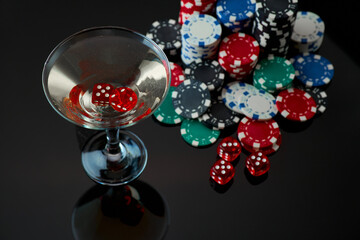 Stack of Casino gambling chips, glass of martini vermouth and red dices isolated on reflective black background