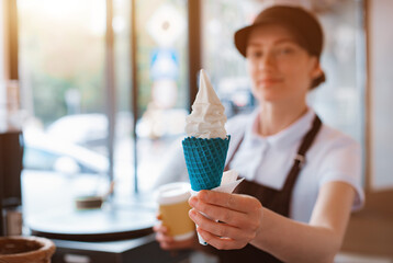 A female seller holds a cone with a twisted ice cream from a vending machine in her hand. Small...