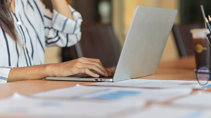 Closeup of businesswoman hand typing on laptop with financial papers