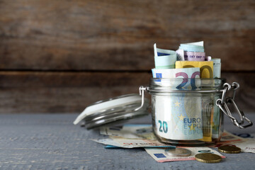 Glass jar full of money on wooden table. Space for text