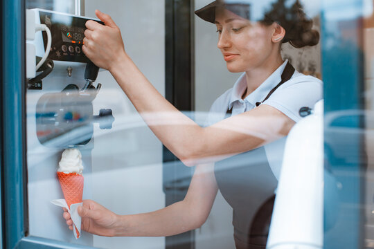 A female seller holds a cone with a twisted ice cream from a vending machine in her hand. Small business and takeaway food, summer food, cool off in the heat