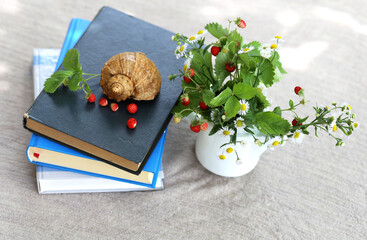Red wild ripe strawberries and a cup with flowers and leaves from a bush of strawberries on a stack of books on a table in the garden