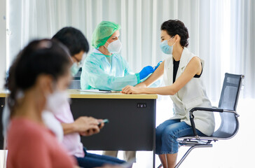 Fototapeta premium Caucasian female professional doctor wears full PPE protection uniform face mask rubber gloves lab coat and hat use syringe needle inject coronavirus vaccine to young woman patient shoulder at desk